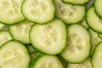 Overlapping cucumber slices fill the frame in a fresh green pattern. The close-up reveals moist seeds and delicate texture, suggesting a crisp, hydrating snack.