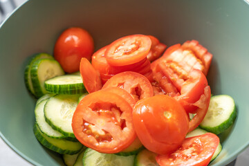 Cucumber and tomato slices are mixed in a bowl. The bright green and red colors create a fresh, healthy salad ready to be seasoned and served.