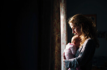 Ternura, protección y la profunda conexión emocional entre madre e hijo. Una mujer sostiene a su bebé junto a la ventana; la suave luz envuelve con ternura su íntimo vínculo maternal.