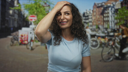 Fototapeta premium Hispanic woman touches her hair with a raised hand on a sunny urban street lined with bicycles; surprise.