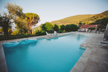 Relaxing scene of a pool area near a hillside location with clear water and lounge chairs under a blue sky in the early evening
