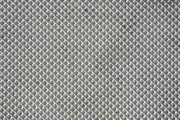A full frame view of a textured grey concrete facade is covered with a repeating pattern of small, conical studs in diagonal rows