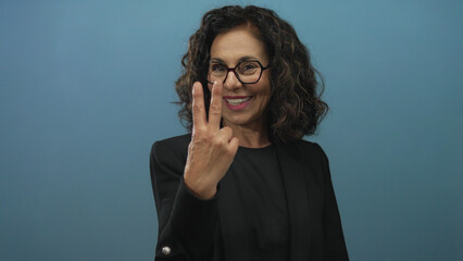 Middle aged hispanic woman makes hashtag sign with fingers against blue studio wall; social media trend connection.