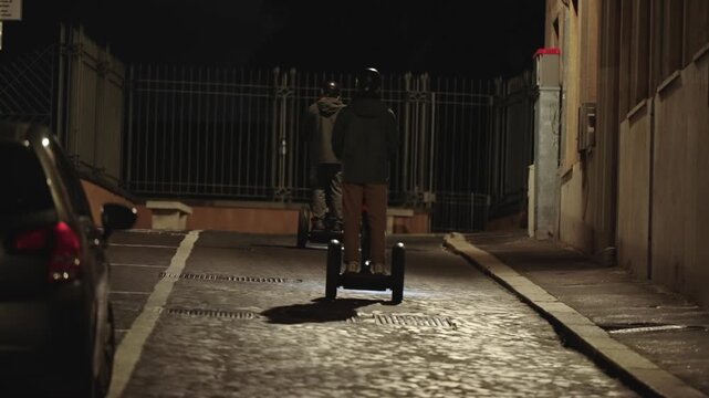 Group of tourists driving Segway scooters on a night tour of Rome, Itlay on dark illuminated alley street, selective focus cinematic shot, slow motion