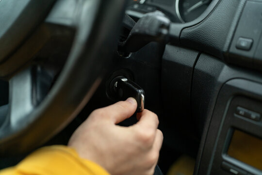 A hand is turning a key in the ignition of a car to start the engine