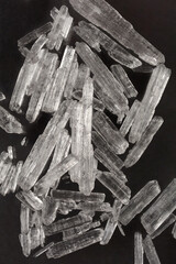 A pile of translucent, colorless menthol crystals is scattered on a dark, reflective surface
