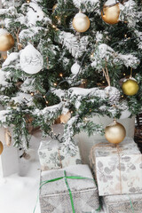 Decorated Christmas tree with golden and white ornaments, sparkling lights, and snow-covered branches, with gifts wrapped in snow. Holiday concept for greeting card.