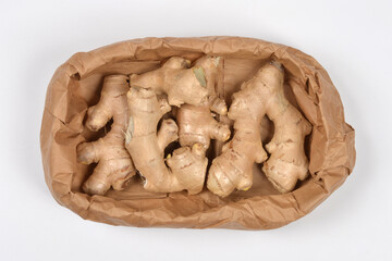An overhead shot of several fresh, unpeeled ginger roots nestled within a brown paper bag, isolated on a clean white background