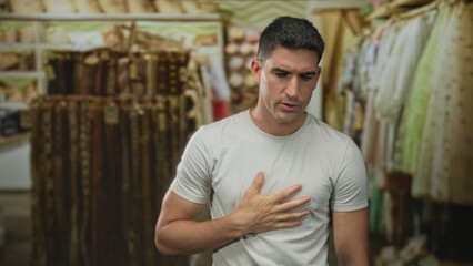 Obraz premium Man clutching chest with bare hand inside a clothing store building, grimacing and hunched near racks of garments; panic medical concern.