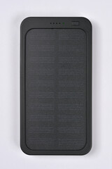 A black, rectangular portable power bank with a segmented solar panel surface and status LEDs is...