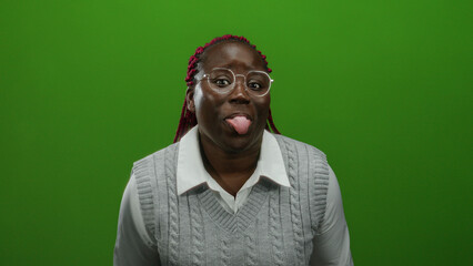Woman with glasses and braided hair playfully sticking tongue out against a vibrant green wall...