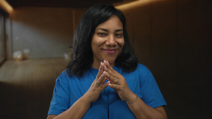 Woman wearing blue shirt smiling steeples fingers in spacious studio; serene calm confidence...