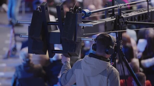 Unrecognizable event operator using camera crane for professional video recording during live audience