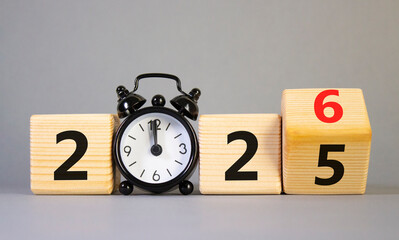 2026 New Year symbol. Businessman turns wooden cube and changes Year 2025 to 2026. Beautiful grey background with Alarm clock. Copy space. Business and 2026 happy new year concept