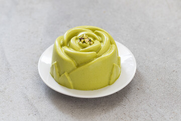 Pistachio cream dessert in the shape of a rose. Decorated with chopped pistachios. Oh a plate. Close up