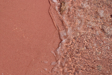 Pink sand beach with gentle waves lapping at the shore creating texture © Svitlofor
