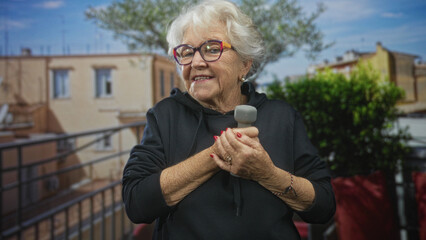 Senior woman holding dumbbell with hands clasped on a building balcony, smiling and exercising for strength and balance; resilience vitality.