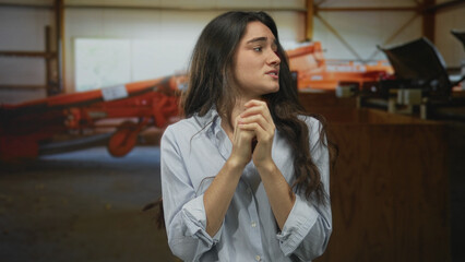 Fototapeta premium Young hispanic woman clasping hands near chest in studio with tense expression; fear vulnerability.