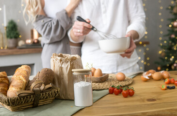 Man whisking ingredients in bowl while woman stands beside him in kitchen. Christmas baking and cooking preparation concept. Cozy holiday home.