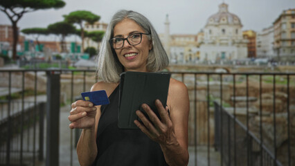 Woman holds tablet and creditcard at ruins, smiling and reading screen while showing hands; serenity.