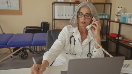 Woman doctor with stethoscope on phone reaching for papers in clinic building office; patient care...