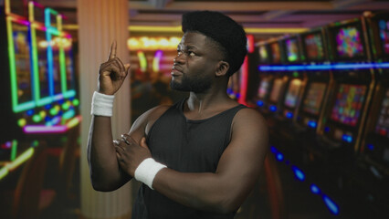 Man with wristband pointing index finger upward and hand on chest near slot machines in casino building; confidence resolve.
