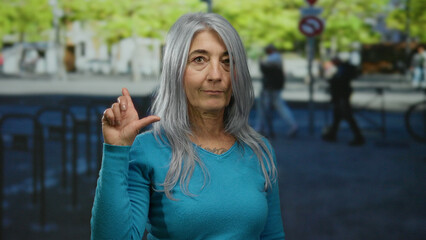 Senior woman with grey hair makes a gesture on a busy street, capturing the lively outdoor urban...