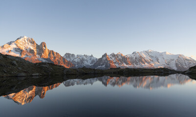 View of a serene lake mirroring snow-capped mountains kissed by the warm glow of the setting sun, Lacs des Cheserys, Auvergne-Rhone-Alpes, France.