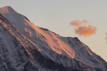 View of snow-capped mountain peaks kissed by the warm glow of sunset, with wisps of clouds drifting by, Chamonix-Mont-Blanc, Auvergne-Rhone-Alpes, France.