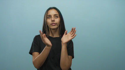 Woman with crossed arms and clapping hands in studio against cyan blue wall, black t shirt and...