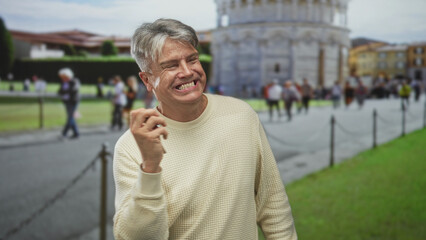 Man holding car keys smiling and gesturing in front of a historic building at a crowded tourist square near the leaning tower of pisa; joy travel memory.