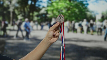 Man holding medal outdoors in city street surrounded by blurred crowd, showcasing achievement and success in a public urban setting.