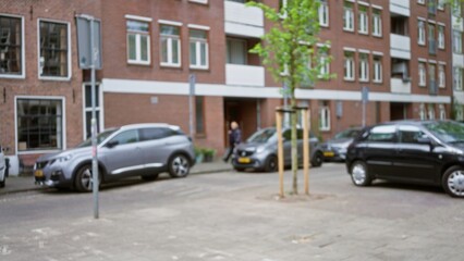 Blurred image of a woman walking in a european city street with cars and buildings in the background, showcasing an urban outdoor environment with defocused bokeh effect.