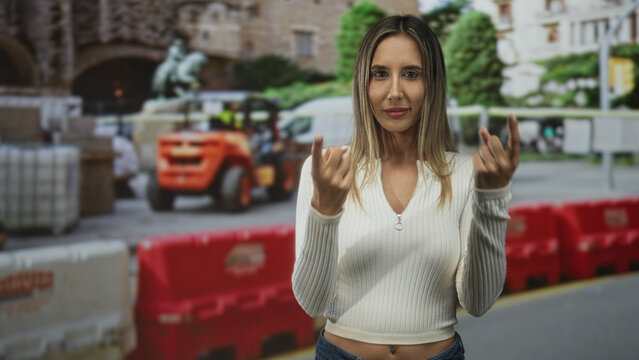 Woman beckoning with fingers and navel piercing visible on street near construction site; playful defiance.