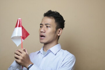 Excited young Asian men celebrate Indonesian independence day on 17 August by holding the Indonesian flag isolated over cream background
