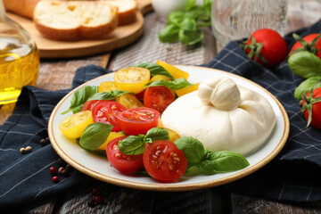 Delicious burrata cheese with basil and tomatoes on wooden table, closeup