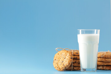 A glass of milk and oatmeal chocolate chip cookies on a light blue background.