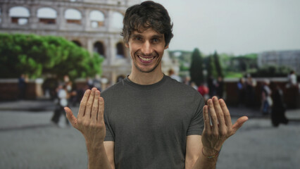 Man smiling beckons with hands in front of colosseum building; travel exploration heritage...