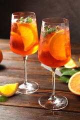 Glasses of refreshing spritzer cocktail and oranges on wooden table