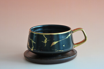 Eine schwarze Tasse Tee im Marmor Design mit Holzuntersetzer