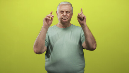 Fototapeta premium Man points finger at camera while holding v with hand over his eye, wearing green shirt in a studio setting; confidence attention.
