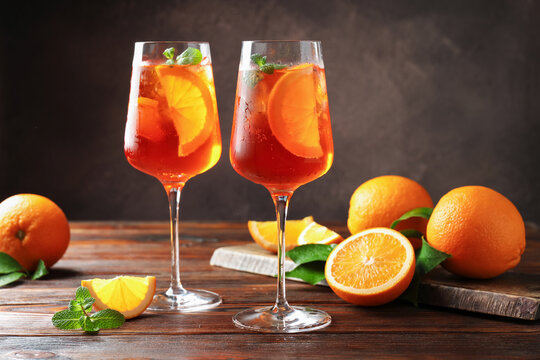 Glasses of refreshing spritzer cocktail and oranges on wooden table