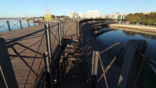 Historic wooden pier in Huelva, Spain, bathed in soft morning light. Industrial heritage meets tranquil coastal scenery and urban skyline. Muelle del Rio Tinto
