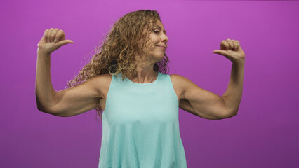 Woman middle age hispanic pointing thumbs to chest showing biceps in studio with playful smirk; confidence defiance.