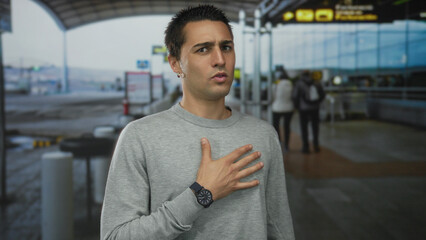 Fototapeta premium Young hispanic man standing outdoors in airport terminal expressing emotions with hand gestures.