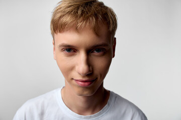 Fototapeta premium Young man with blond hair wearing a white tee, close up face, soft studio lighting, neutral background, calm expression, natural and clean look for fashion or lifestyle projects