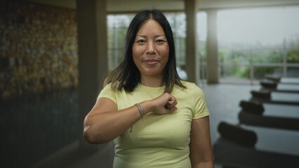 Woman smiling with eyes closed, arm bent across chest in a spa building near indoor pool; calm contentment.