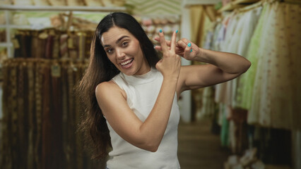 Woman face and hands making hashtag gesture inside a clothing store building surrounded by hanging garments on racks; playfulness.