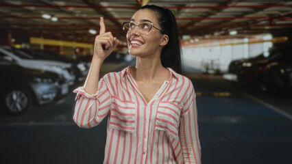 Woman smiling and pointing finger upward to a parked car inside an underground parking building; curiosity.