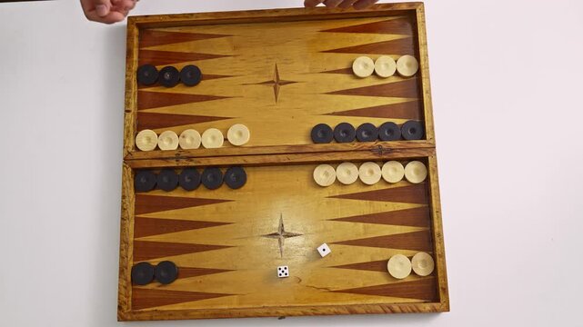 Hands skillfully roll dice and move black and white checkers on a classic wooden backgammon board. Perfect for concepts of strategy, board games, and leisure activities.